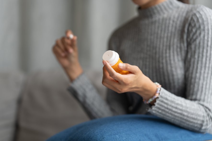 Woman in a grey knit sweater holding a supplement bottle